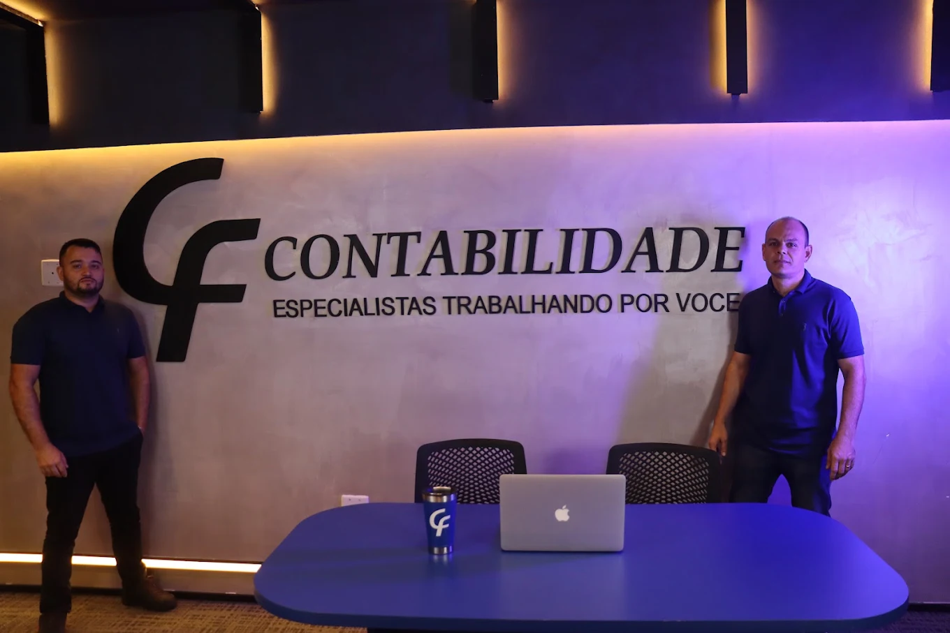 Sócios da CF Contabilidade na sala de reunião, ao lado do logotipo aplicado na parede